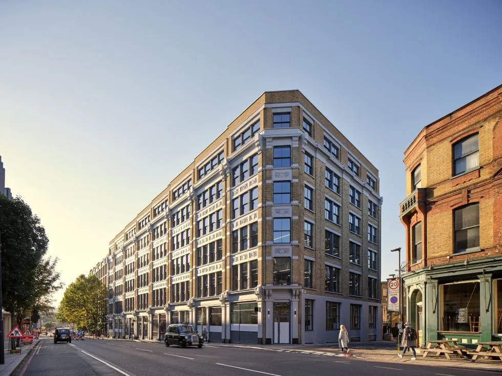 Renovated brick corner building with black-framed windows on a London street, with pedestrians, cars and neighbouring period buildings.