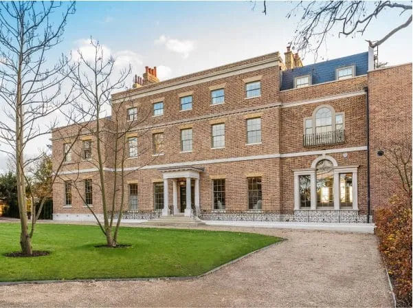 Large Georgian-style brick property with traditional timber windows, arched balcony doors, landscaped lawn and gravel driveway.