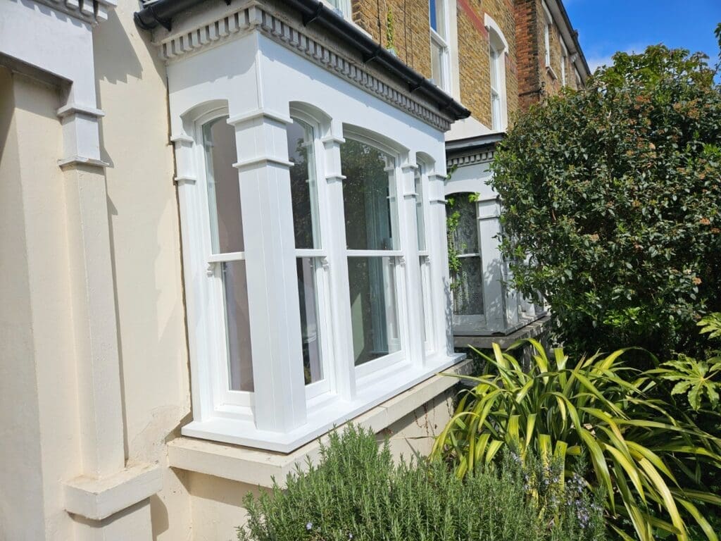 Close-up of a traditional-style bay window with white timber sliding sash windows, showcasing a heritage aesthetic ideal for discussing sash balance systems like lead weights and spiral balances.