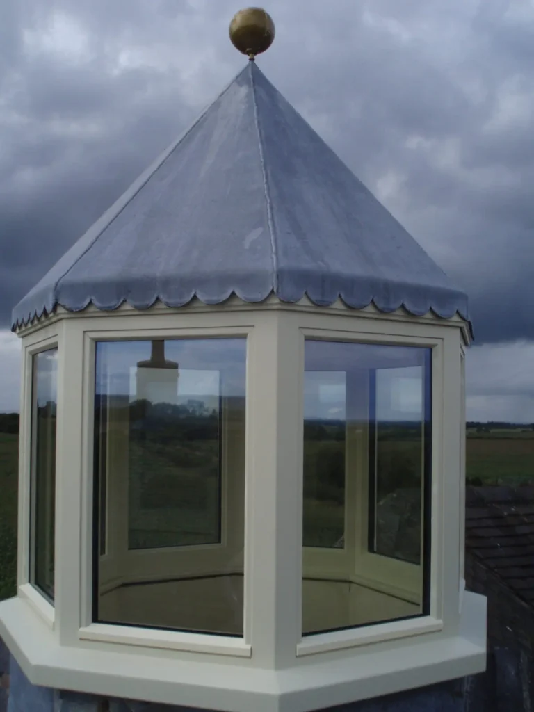 Octagonal roof lantern constructed from Accoya timber with large glazed panels and a scalloped lead roof, designed for an exposed location under dramatic cloudy skies.