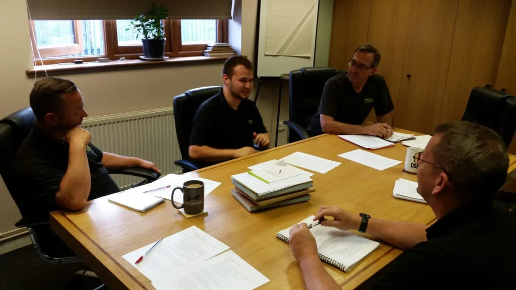 Greg, Gowercroft apprentice and award nominee, sits at the centre of a meeting table with three team members during a quality and health and safety discussion, highlighting the company's commitment to training and apprentice development.