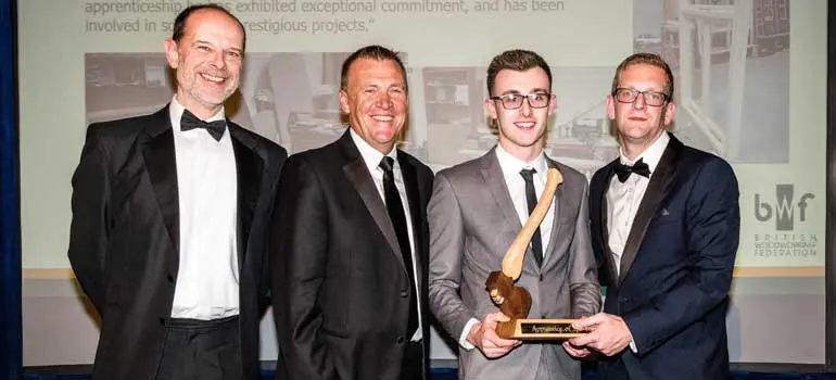 Apprentice wearing grey suit being handed apprentice of the year trophy.