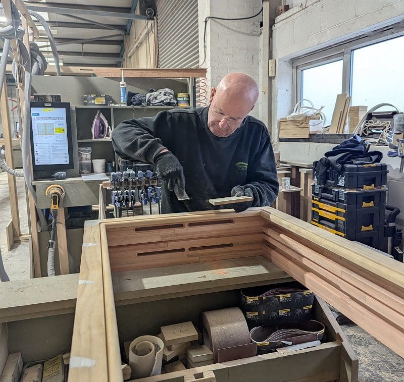 Craftsman working on s timber window frame with a chisel.