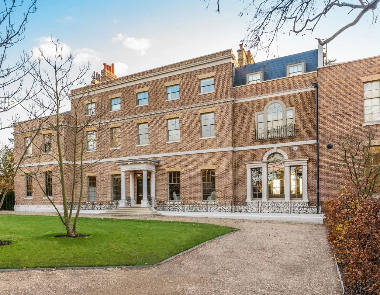 Georgian-style brick building with sash windows, arched doorway and paved entrance path, set behind a lawn and small trees.